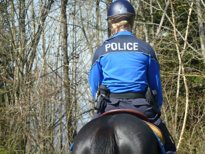 Police cantonale jurassienne - Brigade équestre. Cavalière sur son cheval, de dos