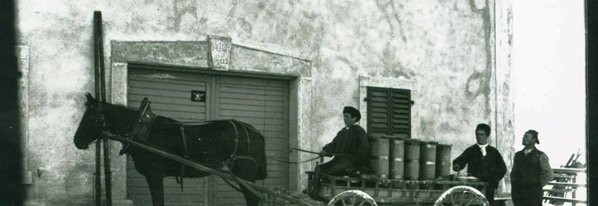3 hommes et un char attelé transportant des tonneaux devant une ferme dont la clef indique AIG 1902 (137 J 496)